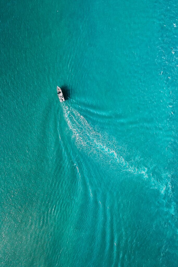 Barco navegando en mar turquesa, visto desde el aire con su estela